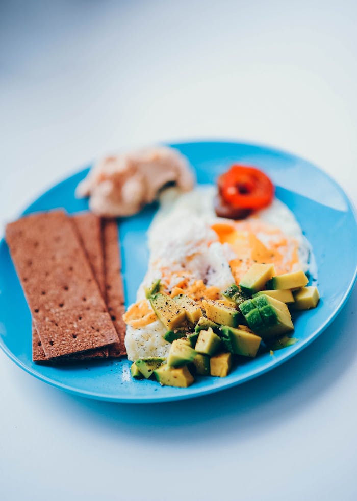 mobile-01 A delectable breakfast plate featuring fried eggs, sliced avocado, and crispy bread crackers.
