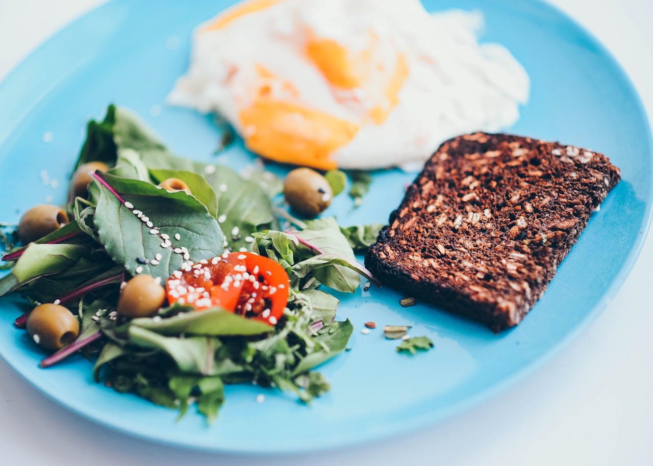 creative-02 A nutritious breakfast plate featuring eggs, rye bread, salad, and olives on a vibrant blue plate.